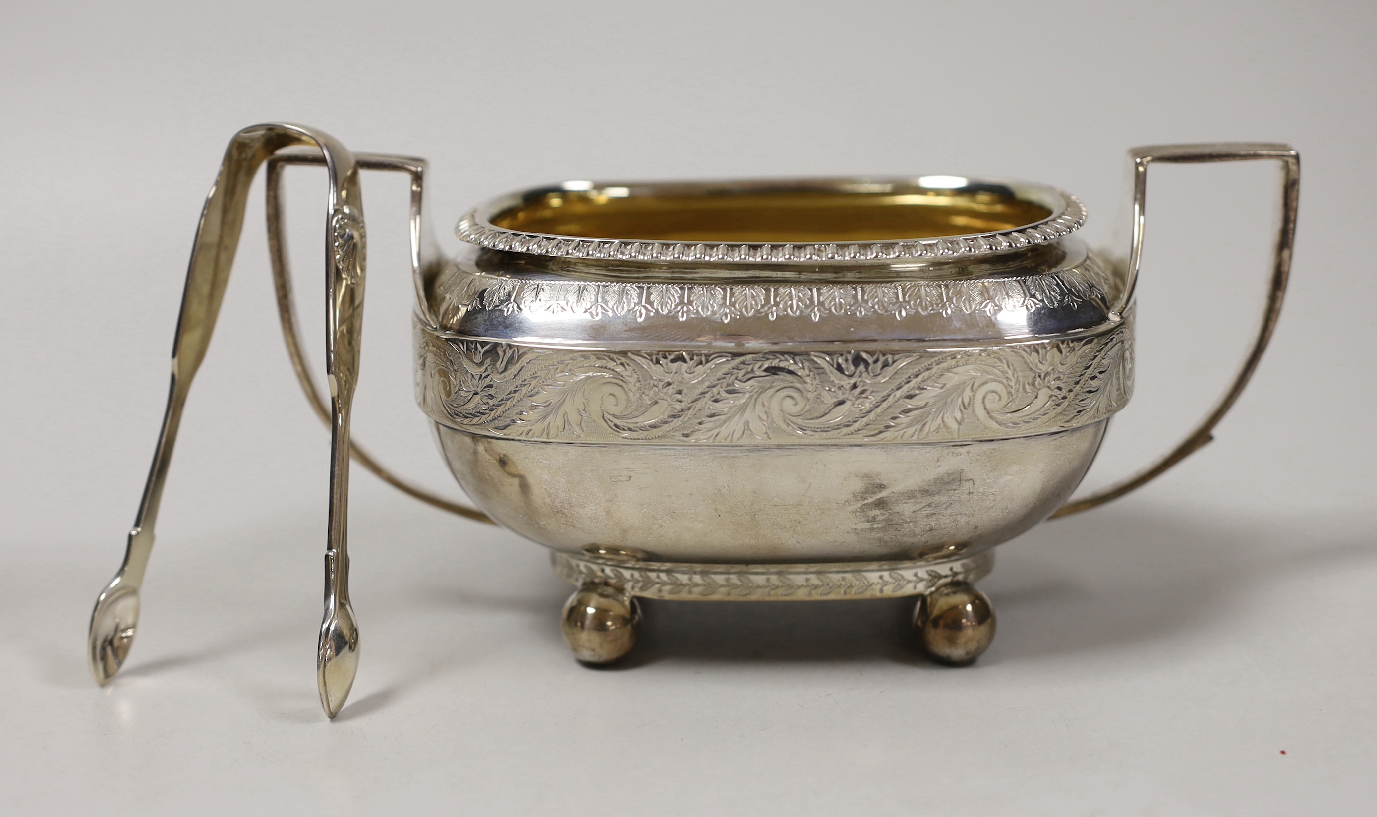 A George III engraved silver two handled sugar bowl, Emes & Barnard, London, 1811, overall width 18.5cm and a pair of Victorian silver sugar tongs, 10.4oz.